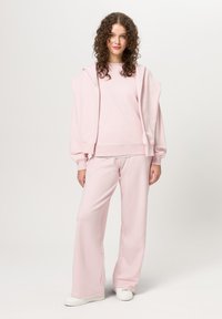 Světle růžová mikina s volným střihem a spadlými rameny, spárovaná s širokými kalhotami ve stejném odstínu, vytvářející celkový soupravu pro domácí nošení.