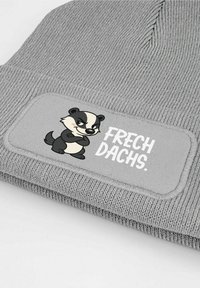 Gray knitted beanie with a textured fabric, featuring a patch with a cartoon badger and the text "FRECH DACHS" in white.