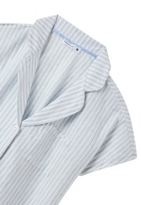 Camicia a maniche corte a righe in tessuto blu chiaro e bianco; presenta un colletto, una tasca e chiusura con bottoni. Texture morbida, design casual.