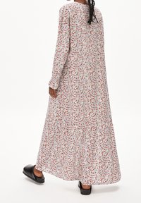 Robe longue fleurie en tissu léger, avec un fond blanc orné de fleurs rouges et bleues, manches longues et silhouette fluide.