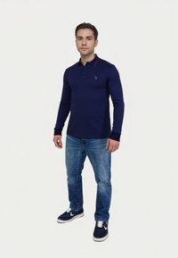 Navy long-sleeve polo shirt with red collar accents, paired with blue jeans and navy sneakers. Features a small logo on the chest.