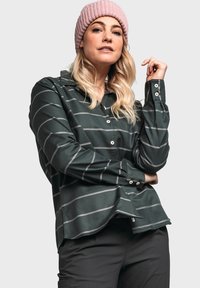 Tmavě zelená košile na knoflíky s bílými horizontálními pruhy, dlouhé rukávy, límec a zakřivený lem. Modelka má na hlavě růžovou pletenou čepici.