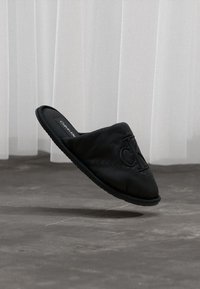 Μαύρο slip-on παπούτσι με επενδεδυμένη υφή, που διαθέτει εξέχον λογότυπο Calvin Klein. Ίσια σόλα και μινιμαλιστικός σχεδιασμός σε φωτεινό φόντο.