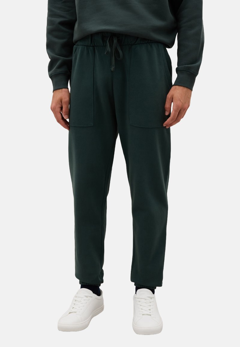 Donkergroene sweatpants met een elastische tailleband, trekkoord en voorzakken, gecombineerd met witte sneakers. Glad textuur van de stof.