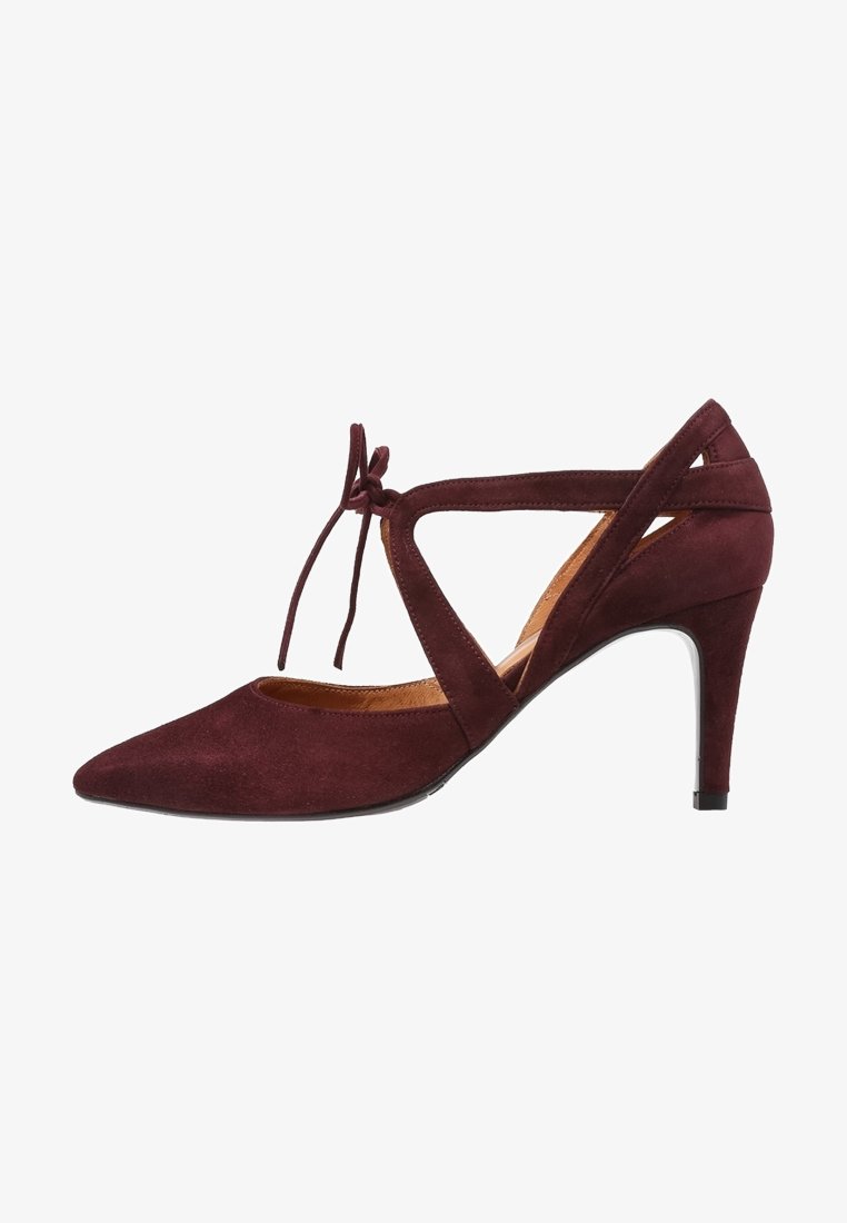Escarpin à talons hauts en daim bordeaux avec bout pointu, lacets autour de la cheville et découpe sur les côtés. Semelle intérieure en cuir lisse et talon noir.