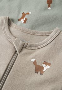 Tissu beige avec des renards imprimés et un détail de fermeture éclair près de l'encolure arrondie d'un vêtement.