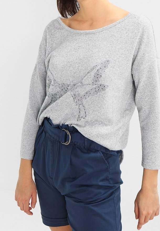 Pull gris à manches longues avec un motif de papillon composé de petits strass, associé à un short bleu marine à taille élastique avec une ceinture.