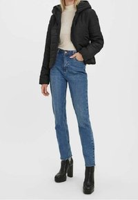 Sort puffervest med hætte, beige ribstrikket trøje, højtaljede blå jeans og sorte platformstøvler med en klodset hæl.