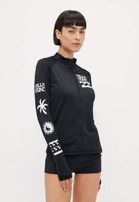 Črn zaščitni rash guard z zadrgo, ki ima na rokavih bele grafične odtise valov, sonca in palm. Gladek, raztegljiv material.