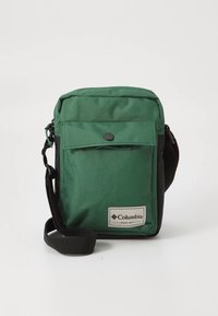 Grønn og svart skulderveske med frontlomme med klaff, laget av stoff, justerbar rem og en tagg med Columbia-logoen.