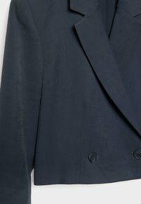 Blazer court bleu marine foncé avec larges revers et deux boutons visibles à l'avant, suspendu sur un fond clair.