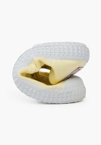 Żółty płócienny sneakers z białą gumową podeszwą, zaokrąglonym czubkiem i przeszyciami. But jest obrócony na bok, pokazując swoje wnętrze.
