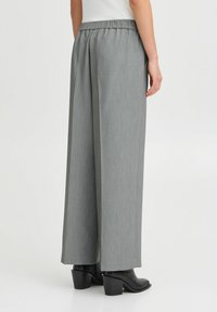 Brede broek in lichtgrijs stoffen met een gemetste patroon, voorzien van een elastische tailleband en gecombineerd met puntige zwarte laarzen.