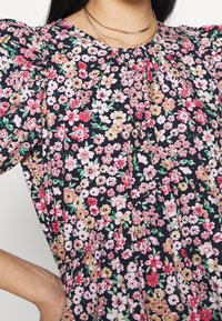 Vestido floral con mangas cortas abullonadas. Fondo oscuro con flores rosas, rojas y amarillas. Tejido suave con detalles fruncidos.