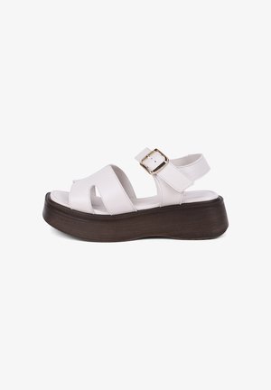 Sandale à plateforme en cuir blanc avec une large bride, une boucle dorée et une semelle épaisse marron, vue de côté sur fond blanc.