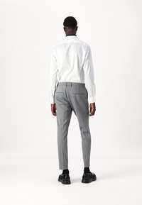 Biała koszula z długim rękawem i czarnym kołnierzykiem, w połączeniu z szarymi, dopasowanymi spodniami. Buty są czarne, z okrągłym noskiem i teksturowaną powierzchnią.