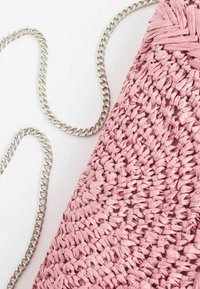 Sac à main tissé rose avec une bandoulière chaîne argentée sur fond blanc, montrant une texture détaillée et un matériau entrelacé.