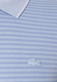 Light blue polo shirt with white horizontal stripes, featuring a textured fabric and a small, embroidered logo on the chest.