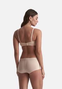 Beige draadloze bh en bijpassende boyshorts, gemaakt van gladde stof. De bh heeft verstelbare bandjes en een haak-en-oogsluiting aan de achterkant.