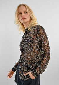 Camicia a maniche lunghe trasparente con stampa floreale nera, caratterizzata da motivi floreali multicolori, colletto e taschino frontale.