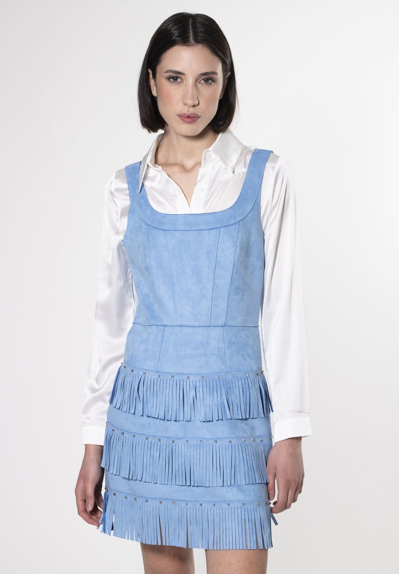 Mini abito in suede blu con scollatura quadrata e dettagli di frange a strati all'orlo, abbinato a una camicia bianca con bottoni sotto.