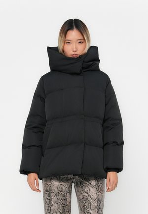 Giacca nera imbottita con colletto alto, caratterizzata da un design squadrato, cuciture visibili e tasche laterali, abbinata a pantaloni con stampa serpente.