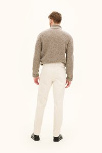 Beige stickad tröja med hög krage och ribbad textur, kombinerad med ljusbeige byxor och svarta skor, sedd bakifrån.