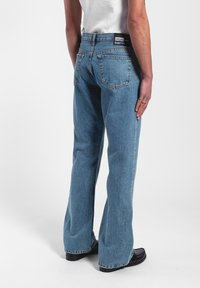 Vaaleansinisiä farkkuja, joissa on rento istuvuus, levenevät lahkeet ja korkea vyötärö. Ominaisuuksiin kuuluu kaksi takataskua ja merkin logolla varustettu vyötärönauha.