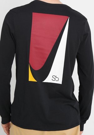 Chemise noire à manches longues avec un grand motif géométrique en rouge, noir, blanc et jaune au dos, comportant un petit texte "Sb.".
