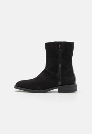 Schwarze Wildleder-Ankle-Boots mit runder Zehenform, glatten schwarzen Akzenten und dezenten Nähten an der Seite. Verfügt über einen niedrigen Absatz und ein minimalistisches Design.