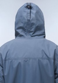 Chaqueta con capucha gris de textura suave, que presenta una costura en la parte trasera y un lazo para el ajuste en la parte superior de la capucha.