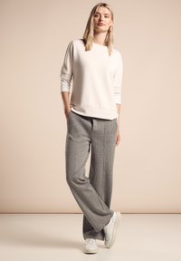 Sweatshirt rose clair à manches trois-quarts, associé à un pantalon large à carreaux gris et des baskets blanches. Texture de tissu lisse.