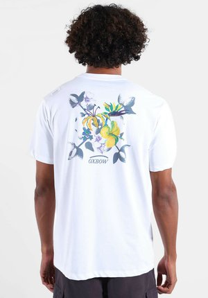 T-shirt en coton blanc avec un dessin floral coloré au dos. Manches courtes et coupe décontractée, avec une petite étiquette logo sur l'épaule.