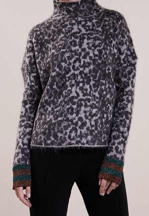 Coltrui met grijs-zwart luipaardprint en bruine en groene gestreepte manchetten, gedragen met een zwarte broek.