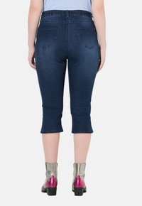 Jeansowe spodnie capri w ciemnoniebieskim kolorze z elastycznym paskiem w talii i dwiema tylnymi kieszeniami, z nogawkami sięgającymi poniżej kolana.