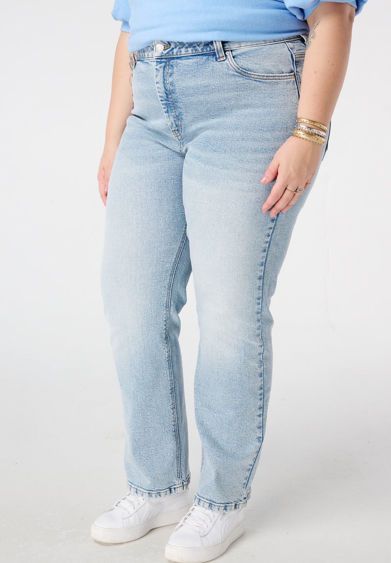 Jean en denim bleu clair avec une coupe droite, taille haute, léger délavage et style à cinq poches. Associé à des baskets blanches.