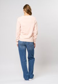 Lichtroze trui met ribbelmanchetten en -zoom, gecombineerd met losse, lichtblauwe jeans. Zachte textuur, casual pasvorm en minimalistisch ontwerp.