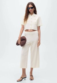 Camisa corta de botón en color crema, con mangas cortas, combinada con pantalones de pierna ancha. Los accesorios incluyen gafas de sol oscuras y un bolso marrón.