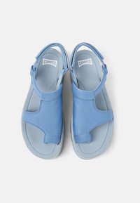 Blue sandals made of soft synthetic material, featuring adjustable straps, padded sole, and a minimalist design. No visible patterns or hardware.