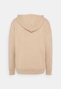 Sudadera con capucha beige de textura suave, que cuenta con un bolsillo canguro y puños acanalados. Diseño simple, sin logotipos ni patrones visibles.