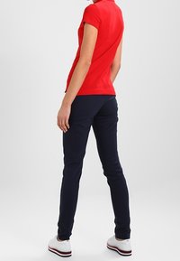 Röd kortärmad polo skjorta i kombination med marinblå smalt passande byxor och vita sneakers med randig sula, sett bakifrån.