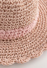 Chapeau en paille tissée de couleur rose clair, avec un corps texturé et un bandeau lisse plissé. Bord festonné avec des détails de tissage complexes.