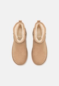 Tan-farbene Wildleder-Ankle-Boots mit einem samtigen, cremefarbenen Innenfutter. Sie verfügen über eine runde Zehenform und eine kleine Zuglasche an der Rückseite. Weiche Textur im gesamten Schuh.