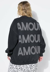 Svart oversized sweatshirt med stor vit "AMOUR" text på ryggen i en vågig stil. Mjukt tyg med ribbad mudd och fåll.