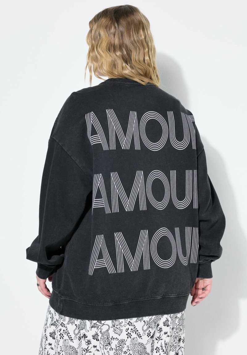 Svart oversized sweatshirt med stor vit "AMOUR" text på ryggen i en vågig stil. Mjukt tyg med ribbad mudd och fåll.