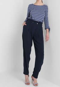 Marina högmidjade byxor med frontveck, i kombination med en långärmad topp i blå och vit rand. Outfitten har öppna klackskor.