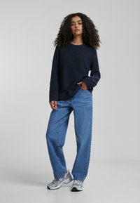 Pull en tricot côtelé marine, coupe décontractée, associé à un jean bleu clair ample et des baskets grises. Design simple, détails minimalistes.