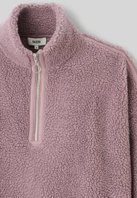 Pull en polaire de couleur lilas clair, avec un col montant, une fermeture éclair mi-zip et une surface texturée et duveteuse. L'étiquette à l'intérieur indique "B2B", taille S.