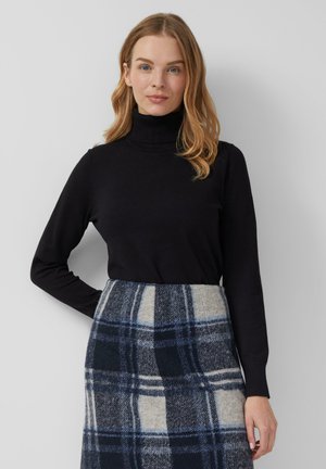 Pull à col roulé noir en textile doux, associé à une jupe à carreaux grise et bleue avec une forme structurée et un motif distinct.
