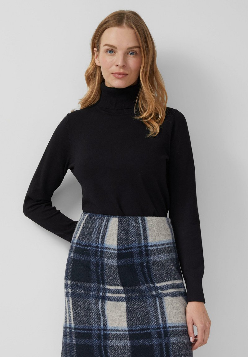Zwarte turtleneck trui van zacht textiel, gecombineerd met een grijs en blauw geruite rok met een gestructureerde vorm en een duidelijk patroon.
